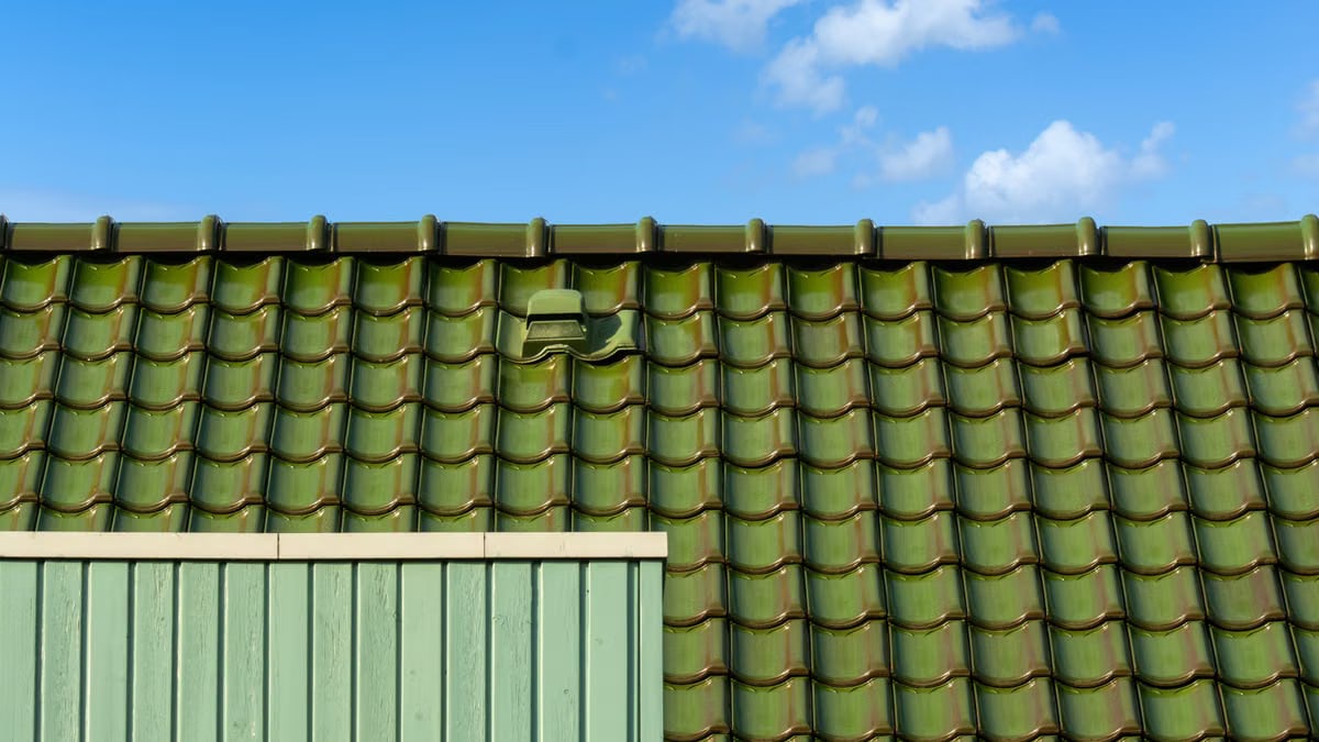 Closeup of a green tiled roof under a bright blue sky, capturing architectural detail and color contrast.