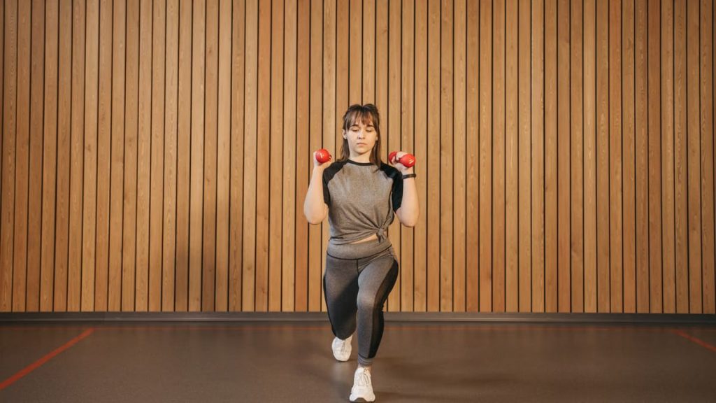 A woman performing lunges with dumbbells in a modern indoor gym setting.