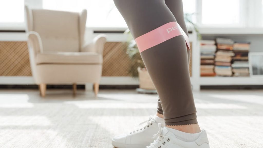 Close-up of legs using a resistance band for stretching exercise indoors.